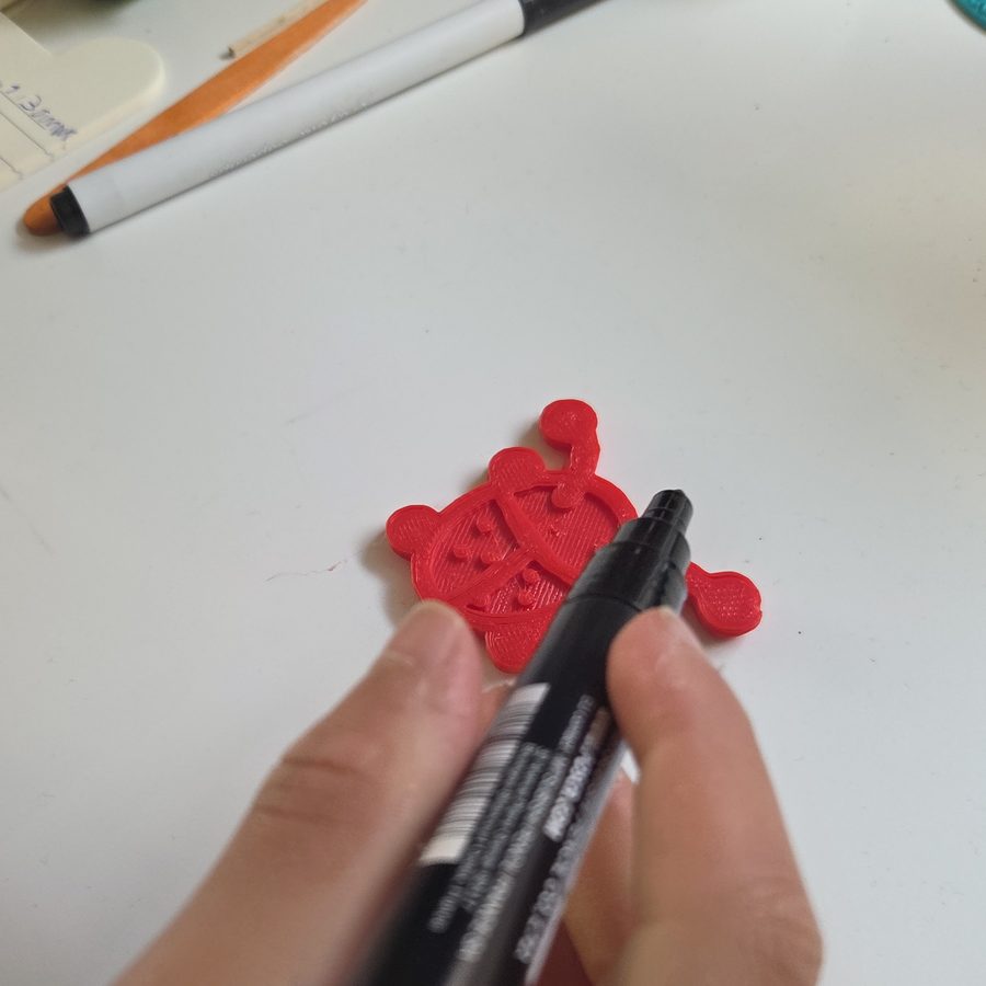 A black paint pen about to go on a red printed ladybug